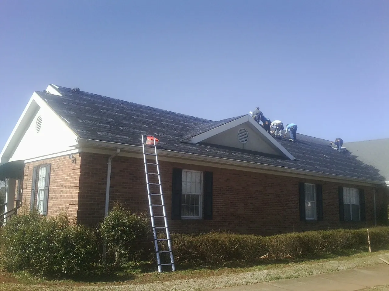 Crew tearing shingles off a brick ranch roof with a ladder set — Emergency Roof Repair work by our crew in Avondale Estates