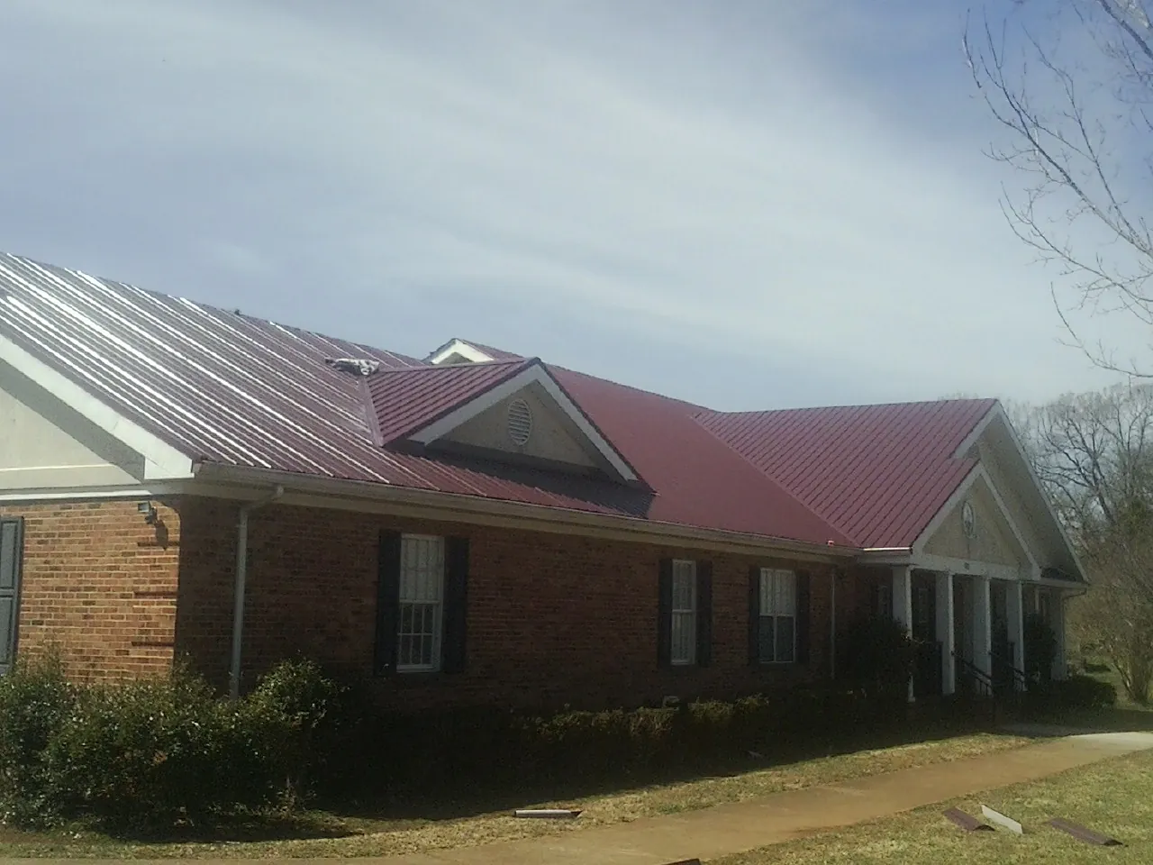 Red metal roof with gabled entries on a long brick building, from a Hail Damage Roof Repair job in Avondale Estates