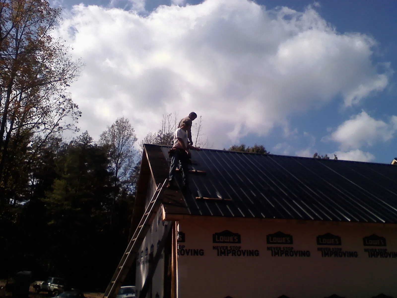 Roofer fastening dark metal panels high against a cloudy sky, from a Roof Inspection job in Avondale Estates
